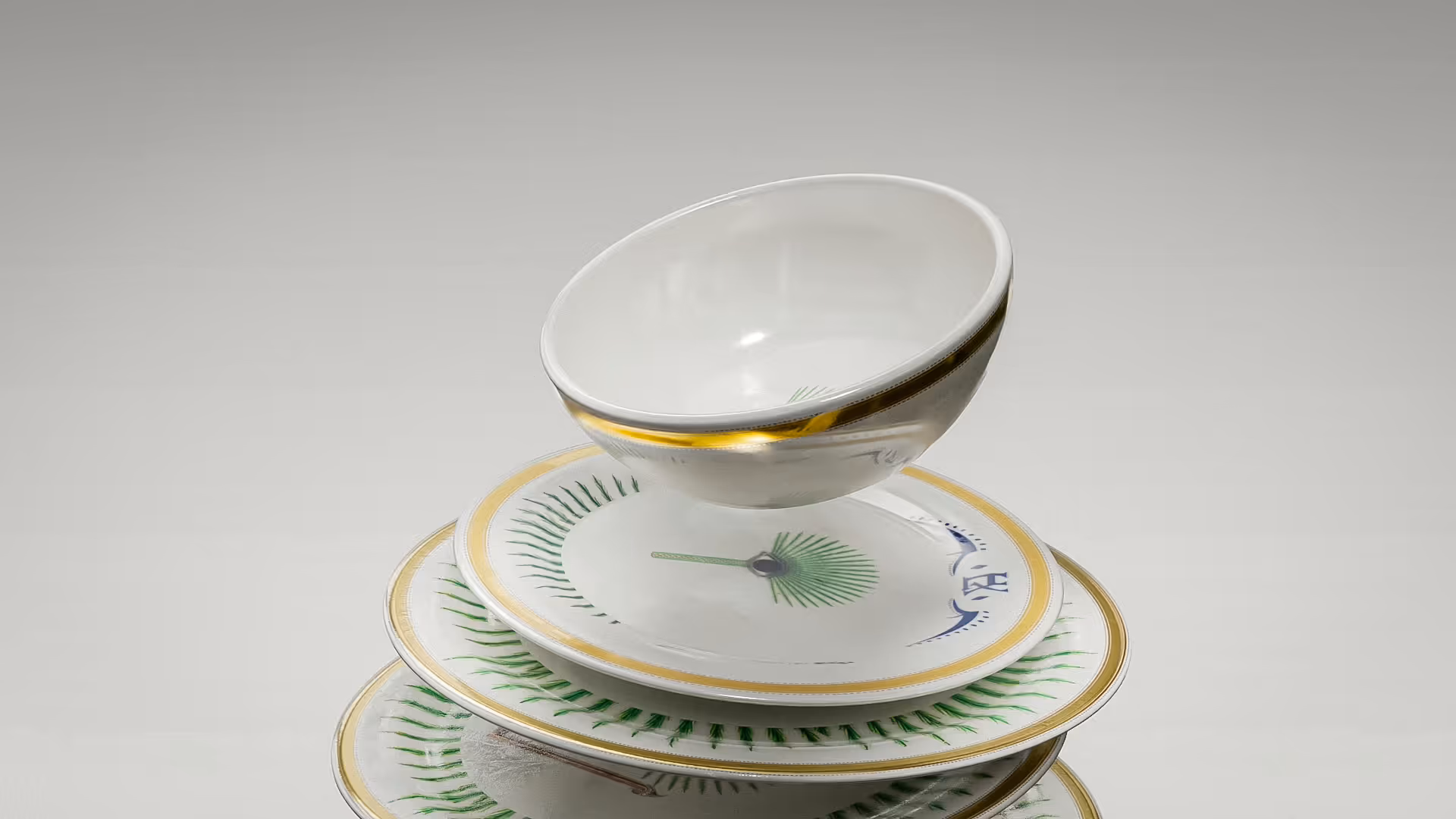 Corona tableware 3D motion graphics by NEA Studio, CGI render of stacked white porcelain plates and bowl with gold trim and green palm leaf pattern on neutral background